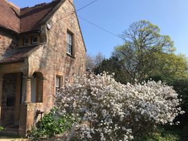 A stone house with a tiled roof next to a large bush with white flowers and trees in the background at Middle Lodge near Taunton