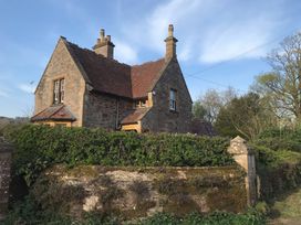 A stone house with a tiled roof and chimneys surrounded by hedges and trees near Taunton