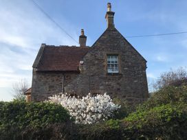 A stone house with two chimneys surrounded by green bushes and a white flowering shrub near Taunton