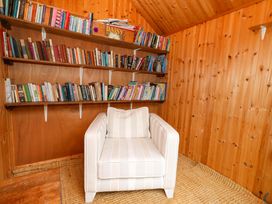 A reading room with a bookshelf and a white chair at Garden Retreat in Swanage