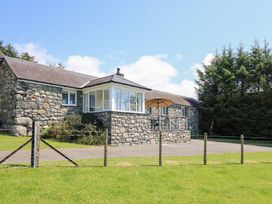 A house with a stone wall and deck in a green space at Ysgubor Newydd Parc Isaf Dyffryn Ardudwy