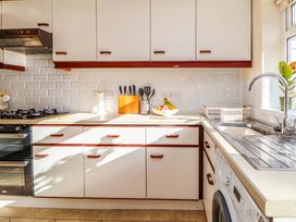 A kitchen with white cabinets a gas stove a sink a fruit bowl and utensils at Green View in Llangollen