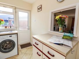 A utility room with a washing machine flowers on the windowsill and a countertop with maps and a flower vase at Green View in Llangollen