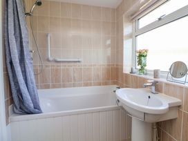 A bathroom with a bathtub shower sink flowers and a mirror at Green View in Llangollen