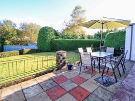 An outdoor patio with a table umbrella and chairs next to a lawn with trimmed hedges at Green View in Llangollen