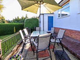 A patio area with a glass table and six chairs under a large umbrella next to a house with a blue door and garden at Green View in Llangollen
