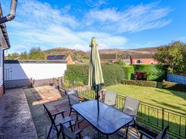 A patio with a glass table and five chairs with a closed umbrella in a garden at Green View in Llangollen