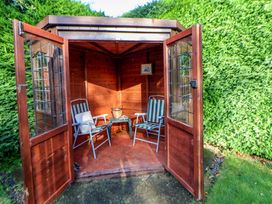An outdoor wooden gazebo with two chairs a small table a basket and green hedge in the background at Green View in Llangollen