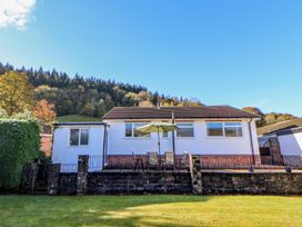 A white house with a patio table and umbrella in front of a grassy yard and trees at Green View in Llangollen