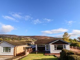 A front view of a single-story house with a lawn and neighboring house with hills in the background at Green View in Llangollen