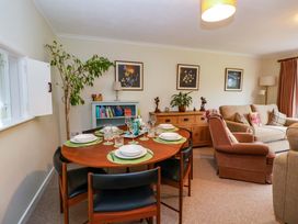 A dining area with a set table and six chairs next to a living room with armchairs and a sofa at Green View in Llangollen