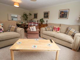 A living room with beige sofas a coffee table with coasters a brown armchair and framed pictures on the wall at Green View in Llangollen