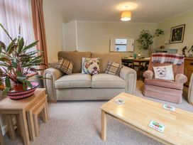 A living room with a beige sofa and armchair with dog-themed cushions a wooden coffee table with coasters and a plant on nested side tables at Green View in Llangollen