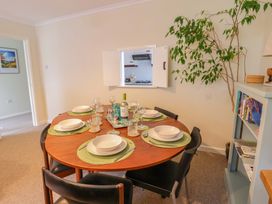 A dining room with a round wooden table set for six with plates and glasses a plant and bookshelf at Green View in Llangollen