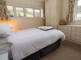 A bedroom with a bed with white linens a wardrobe and dresser with floral curtains at Green View in Llangollen