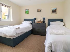 A bedroom with two single beds a black chest of drawers with two lamps and a basket with a stuffed toy and framed pictures on the wall at Green View in Llangollen