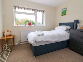 A bedroom with a single bed white bedding blue headboard a window with toys a wooden side table and a dark dresser at Green View in Llangollen