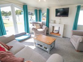 A living room with armchairs a sofa a coffee table a wall-mounted television and teal curtains at 13 Gosling in Cayton Bay