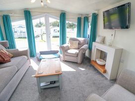 A living room with grey sofas a wooden coffee table a wall mounted tv and turquoise curtains at 13 Gosling in Cayton Bay