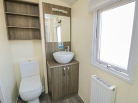 A bathroom with a toilet a wooden cabinet with basin and mirror and a window at 13 Gosling in Cayton Bay
