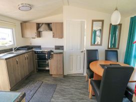 A kitchen with wooden cabinets a stove and a dining area with a round table and four black chairs at 13 Gosling in Cayton Bay