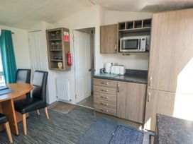 A kitchen area with wooden cabinets dining table with black chairs and a microwave oven at 13 Gosling in Cayton Bay