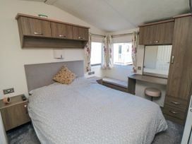 A bedroom with a bed pillow nightstands overhead cabinets a dressing table a mirror and windows with floral curtains at 13 Gosling in Cayton Bay