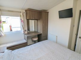A bedroom with a bed, window, bench seat, wooden wardrobe with mirror and stool, and a wall-mounted television at 13 Gosling in Cayton Bay