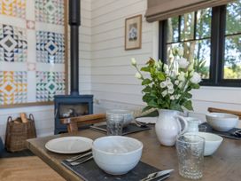 A dining table set with bowls glasses and a white pitcher with flowers by a window and a stove in a room at Walden Lodge in Tresillian Wood near Llantwit Major
