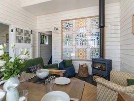 A living room with a wood stove a green armchair a patterned armchair a bean bag and a dining table with dishes and flowers at Walden Lodge in Tresillian Wood near Llantwit Major