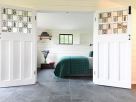 A bedroom with a bed covered in a green and blue blanket a vase with flowers on a chest and decorative glass paneled doors at Walden Lodge in Tresillian Wood near Llantwit Major