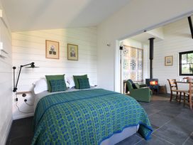 A bedroom with a blue and green bedspread and green pillows next to a sitting area with a wood stove at Walden Lodge in Tresillian Wood near Llantwit Major