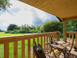 A wooden porch with a table and chairs overlooking a grassy field and trees at Walden Lodge in Tresillian Wood near Llantwit Major