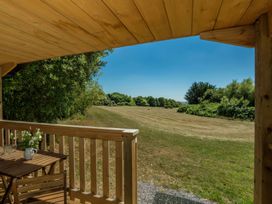 A wooden porch with a table and chairs overlooking a grassy field and trees at Walden Lodge Tresillian Wood near Llantwit Major