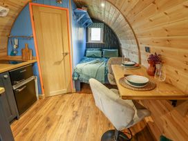 An interior of a small curved wooden room with a bed, a kitchenette, and a wooden dining table with two chairs at Hobhole in Keal Cotes near East Kirkby