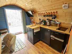 A small kitchen area with a wooden countertop black cabinets a sink hanging mugs a kettle a mini fridge and an open door showing outdoors at Hobhole in Keal Cotes near East Kirkby