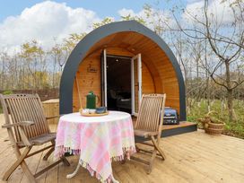 A wooden outdoor deck with a round table covered with a cloth and two wooden chairs in front of a curved wooden cabin at Hobhole in Keal Cotes near East Kirkby