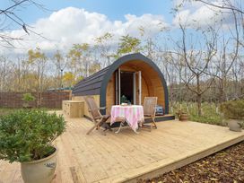 A wooden pod with open double doors on a wooden deck with two chairs and a table with a pink tablecloth surrounded by trees at Hobhole in Keal Cotes near East Kirkby