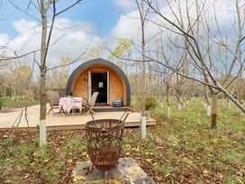 A wooden pod with a table and chairs on a deck in a wooded area with a metal fire pit in front at Hobhole in Keal Cotes near East Kirkby