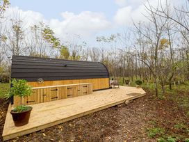 A wooden cabin with a black roof and a wooden deck surrounded by leafless trees at Hobhole in Keal Cotes near East Kirkby