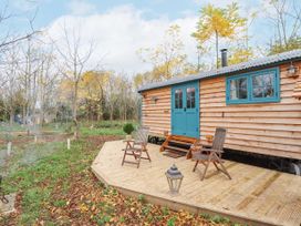 A wooden cabin with teal doors and windows on a wooden deck with two chairs and a lantern surrounded by trees and grass at Catchwater in Keal Cotes near East Kirkby