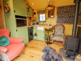 A small kitchen area with green cabinets a red armchair floral upholstered chair a wood stove and a wooden floor at Catchwater in Keal Cotes near East Kirkby