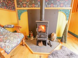 A wood burning stove with fire lit near a patterned armchair and decorative items at Catchwater Keal Cotes near East Kirkby