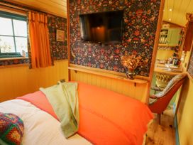 A small bedroom with a bed covered with an orange blanket a wall-mounted tv and a chair next to a kitchen door at Catchwater in Keal Cotes near East Kirkby