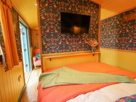 A bedroom with a wall-mounted television a bed with orange and green blankets and floral wallpaper at Catchwater Keal Cotes near East Kirkby
