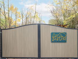 A closed beige and black gate with a sign that reads fen end surrounded by trees