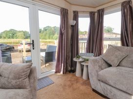 A seating area with beige sofas and side tables near glass doors and windows with curtains at Ashcroft in Warton Lancashire