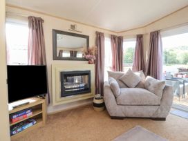 A living room with a beige armchair next to windows with purple curtains and a fireplace with a mirror above it at Ashcroft in Warton Lancashire