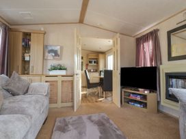 A living room with a sofa rug and tv with a view through double doors to a dining area with chairs and a kitchen at Ashcroft in Warton Lancashire