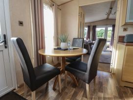 A dining area with a round wooden table and three black chairs near a window and door at Ashcroft in Warton Lancashire